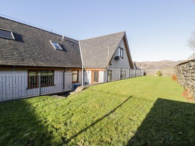 A fenced yard with grass next to a house with a sloped roof and stone wall at Y Tylwyth in Blaenau Ffestiniog