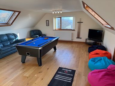 A game room with a pool table blue felt with balls and cues a black television on a stand bean bags in various colors two leather sofas wooden floor and two skylights at Y Tylwyth in Blaenau Ffestiniog