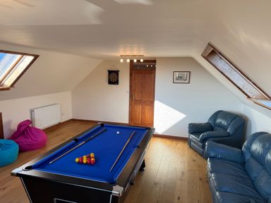 A game room with a pool table two blue leather sofas bean bags a dartboard and wooden door at Y Tylwyth in Blaenau Ffestiniog
