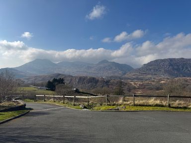 A paved road with a wooden fence alongside grassy land and mountains in the background at Y Tylwyth in Blaenau Ffestiniog