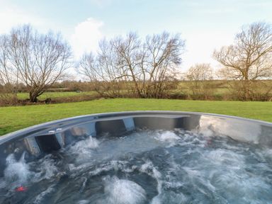 An outdoor hot tub with bubbling water overlooking grass and leafless trees at Otter's View in South Luffenham near Edith Weston