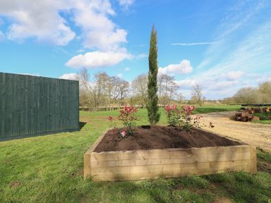A raised wooden planter with soil and plants next to a green fence in a grassy outdoor area at Otter's View in South Luffenham near Edith Weston