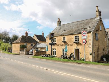 A stone building with outdoor seating and road signs in front at Otters View in South Luffenham near Edith Weston