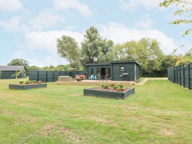 A garden with a wooden deck and outdoor furniture beside a small dark green wooden building at Otter's View in South Luffenham near Edith Weston