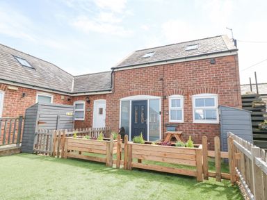 A brick house with a fenced garden and artificial grass at Pine Cottage in Dinas Dinlle