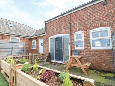 A brick house exterior with a black door wooden picnic table and planters with plants at Pine Cottage in Dinas Dinlle