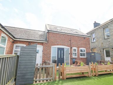 A brick house with a dark blue door and small garden beds with plants in front at Pine Cottage in Dinas Dinlle