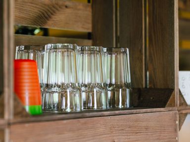 A set of upside down clear drinking glasses and a stack of red and green plastic cups on a wooden shelf at Oak Stockland near Dalwood