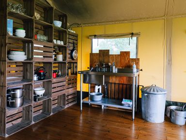 A kitchen area with wooden shelves holding dishes and pots and a metal sink with a trash can at Oak in Stockland near Dalwood