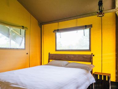 A bedroom with a wooden bed and white bedding inside a yellow tent at Oak Stockland near Dalwood