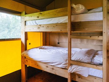 A wooden bunk bed with white bedding inside a tent with yellow and brown walls at Oak Stockland near Dalwood
