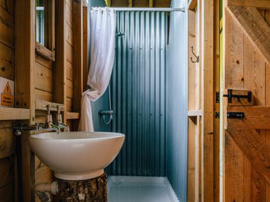 A bathroom with a sink on a wooden stump a shower with a white curtain and wooden walls at Oak in Stockland near Dalwood