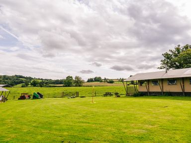 A grassy field with a large tent on the right a picnic table and toy tractors on the left at Oak Stockland near Dalwood
