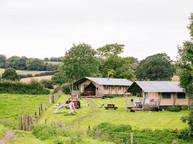 Two large canvas tents with porches on a grassy field with picnic tables near Oak in Stockland near Dalwood