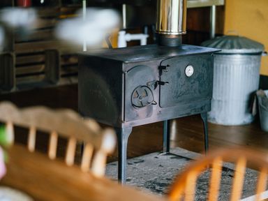 A black wood burning stove with a metallic chimney pipe in a room with wooden floors and chairs at Beech in Dalwood