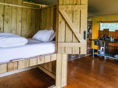 A room with a wooden bed with white bedding and a kitchen area with a metal sink and utensils at Beech in Dalwood