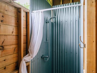 An outdoor shower with a white curtain wooden walls and corrugated metal panels at Beech in Dalwood