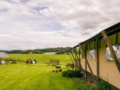 A grassy outdoor area with a large tent structure picnic tables and a children's play area at Beech in Dalwood