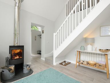 A room with a wood stove fire and a stairway with a console table underneath at Otters Leap in Bideford