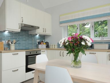 A kitchen with blue tile backsplash white cabinets a dining table and a vase of flowers at Otters Leap in Bideford