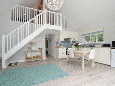 A kitchen with dining table and chairs under stairs with railing at Otters Leap in Bideford