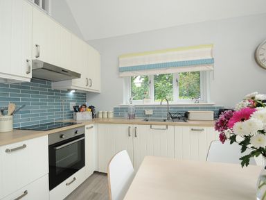 A kitchen with white cabinets blue tiled backsplash a built-in oven a window over the sink and a table with flowers at Otters Leap in Bideford