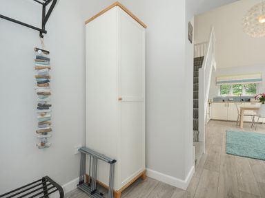 A hallway with a white cabinet a staircase to the right and a view into a kitchen with a dining table and chairs at Otters Leap in Bideford