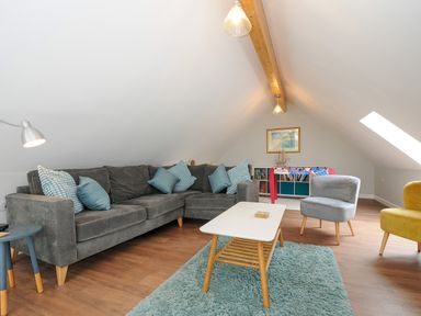 A living room with a grey sectional sofa and blue cushions a white coffee table on a blue rug and a small foosball table at Otters Leap in Bideford