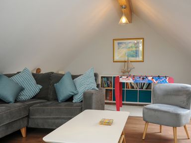 A living room with a grey sofa and blue cushions a white coffee table a grey chair a foosball table and a bookshelf at Otters Leap in Bideford