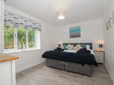 A bedroom with a double bed pillows bedside tables lamps and a window with patterned blinds at Otters Leap in Bideford