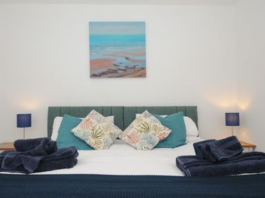 A bed with patterned pillows and folded towels with table lamps on wooden bedside tables at Otters Leap in Bideford