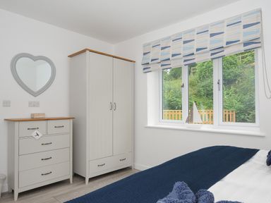 A bedroom with a wardrobe and chest of drawers next to a window with a model sailboat at Otters Leap in Bideford