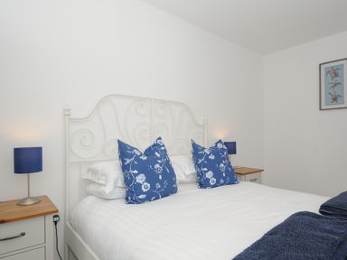 A bedroom with a white metal bed frame blue floral pillows blue lamps on wooden bedside tables and a turtle picture on the wall at Otters Leap in Bideford