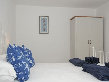 A bedroom with blue floral pillows on a white bed and a wardrobe at Otters Leap in Bideford
