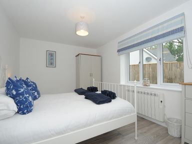A bedroom with a white metal bed, blue floral pillows, folded towels on the bed, a wardrobe, window with striped blind and a radiator at Otters Leap in Bideford