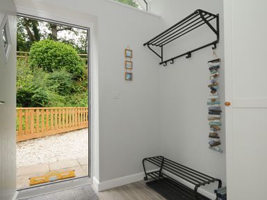 An entryway with a black metal coat rack and shoe rack next to a door opening to a garden at Otters Leap in Bideford