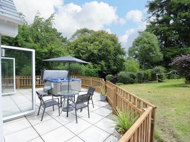 A patio area with a round table with umbrella and four chairs next to a hot tub and garden at Otters Leap in Bideford