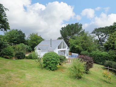 A small white house with large windows surrounded by greenery and bushes at Otters Leap in Bideford