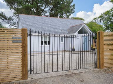 A white house with a slate roof behind a black iron gate and wooden fencing at Otters Leap in Bideford
