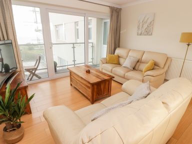 A living room with two beige leather sofas a wooden coffee table a TV on a wooden stand sliding glass doors leading to a balcony with chairs and plants at 54 Croft Court in Tenby