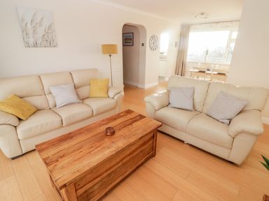 A living room with two beige sofas a wooden coffee table and a dining table near a window at 54 Croft Court in Tenby