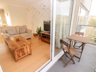 A living room with beige sofa wooden coffee table television and plant opening to balcony with wooden table and chairs at 54 Croft Court in Tenby