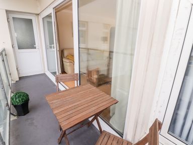 A balcony with a wooden table and chairs along with a potted plant and a view into a living room at 54 Croft Court in Tenby
