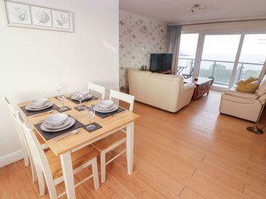 A dining table set with plates and glasses next to a living room with leather sofas and a TV by sliding glass doors at 54 Croft Court in Tenby