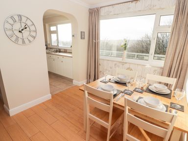 A dining area with a wooden table set for four and a kitchen visible through an archway at 54 Croft Court in Tenby
