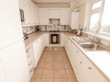 A kitchen with white cabinets a tiled floor a stainless steel sink an oven a gas stove and a window at 54 Croft Court in Tenby