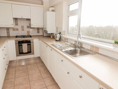 A kitchen with white cabinets a gas stove an oven a sink and a window at 54 Croft Court in Tenby