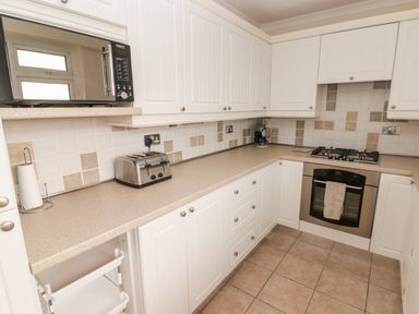 A kitchen with white cabinets a microwave toaster stove oven and tiled floor at 54 Croft Court in Tenby