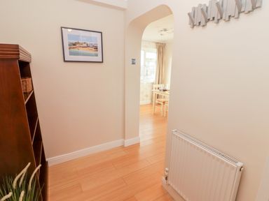 A hallway with wooden flooring radiator bookshelf and a framed picture on the wall at 54 Croft Court in Tenby