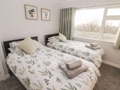 A bedroom with two single beds with floral bedding and folded towels near a window at 54 Croft Court in Tenby